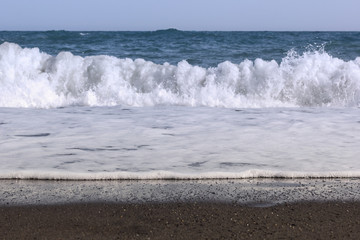 white splashes of waves in the sea rolling on the sandy shore