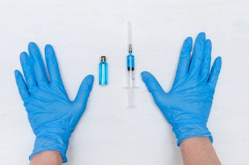 Hands in medicinal gloves and syringe with blue liquid medicine on the doctor table background.