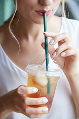Cropped image of young woman enjoying drinking refreshing iced tea with straw