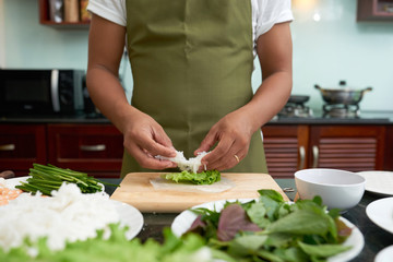 Hands of person making healthy spring rolls with fresh green vegetables