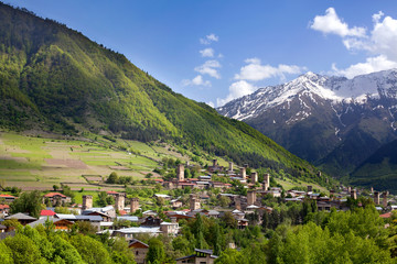 Ushguli village in Georgia, Svaneti region, ancient towers on a green hill high Caucasian mountains, mountain peaks in the snow, blue cloudy sky background