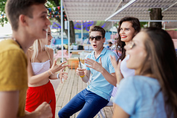 A company of good-looking friends laughing, drinking yellow cocktails and socialising at the bar in the nice summer cafe. Cheers. Entertainment, having good time. Friendship.