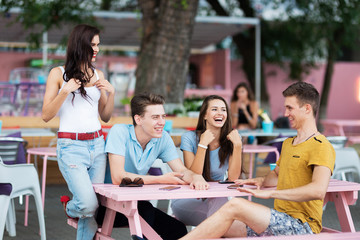 A company of good-looking friends is laughing, socialising and sitting at the table in the nice summer cafe. Entertainment, having good time. Friendship.
