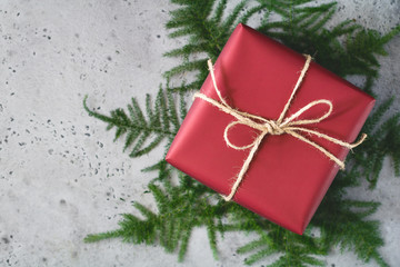 Christmas gift box in a red wrapping paper is tied of twine among winter decoration. Flat lay, top view, copy spce.