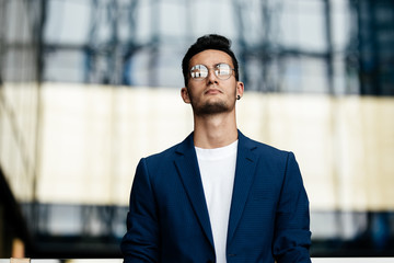 Architect in glasses dressed in stylish clothes stands on the background of a modern glass building