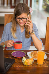 Woman using cellphone and laptop inside house and having a breakfast.