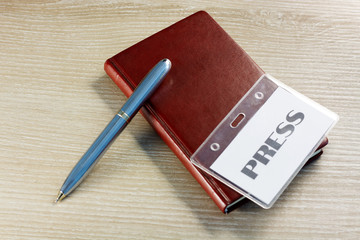 brown notebook with pen and press badge on office desktop