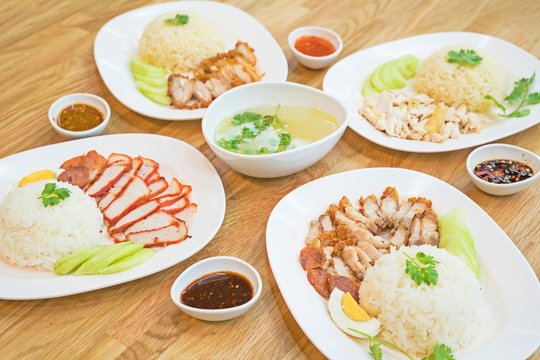 Rice with roasted red pork + Crispy roasted belly pork chinise style on rice + Hainanese chicken rice , Thai gourmet steamed chicken with rice with soup. top view thai food on wooden table.