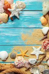 sea rope with many different sea shells on the sea sand on a blue wooden background. Top view