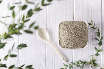 Ceramic bowl with green clay powder and fresh eucalyptus leaves on white background. Concept of...