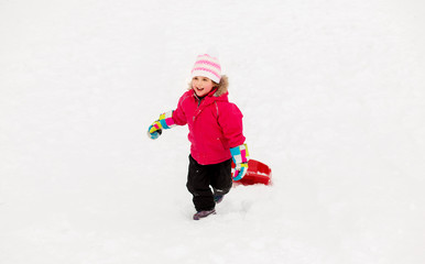 childhood, sledging and season concept - happy little girl with sled climbing snow hill in winter