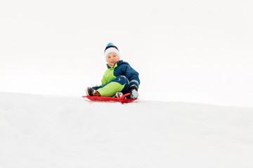 Fototapeta na wymiar childhood, sledging and season concept - happy little boy sliding on sled down snow hill outdoors in winter