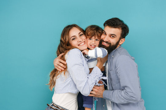 A Happy Family On Blue Studio Background. The Father, Mother And Son Posing Together