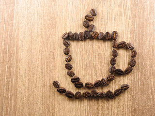 The coffee beans are arranged in a shape of a cup of hot coffee isolated on a brown wood background.Beans can be made into drinks and beverages,like latte,cappuccino, espresso.creative picture,image.