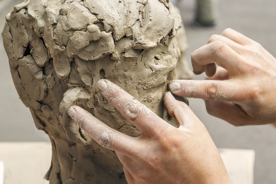 sculptor creates a bust and puts his hands clay on the skeleton of the sculpture. Close-up