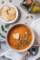 top view of rusks, bottle of olive oil and bowl with pumpkin cream soup with seeds on table