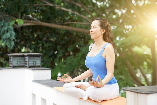 Middle-aged Asian woman meditating outdoors on sunny morning