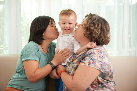 Happy lesbian couple kissing their son on both cheecks
