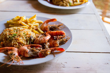 Shrimps on white plate over wooden table, served with rise and french fries, top view. Seafood concept.Selective focus.