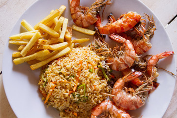 Shrimps on white plate over wooden table, served with rise and french fries, top view. Seafood concept.Selective focus.