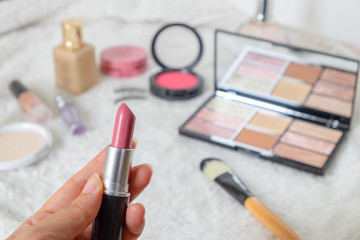 Woman hand holding pink lipstick. Beauty cosmetic products and Various Make up accessories on the white fur background with copy space for your text. Concept of Beauty Knolling.