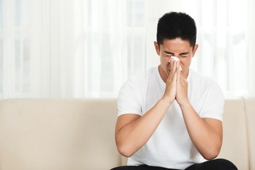 Young mixed-race man using paper tissue to blow his nose