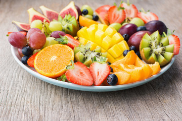 Assorted fruits, strawberries blueberries, mango orange, grapefruit, banana papaya apple, grapes, kiwis on the grey wood background, copy space for text, selective focus