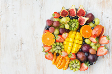 Variety of cut fruits and berries platter, strawberries blueberries, mango orange, apple, grapes, kiwis on the white wood background, copy space for text, vertical, top view, selective focus