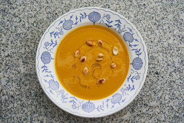 Top view on delicious creamy pumpkin soup made from hokaido pumpkin with roasted seeds and olive oil served in the rustic deep plate on the grey granite stone table.