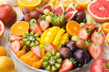 Variety of cut fruits and berries platter, strawberries blueberries, mango orange, apple, grapes, kiwis on the white wood background, copy space for text, vertical, close up, selective focus