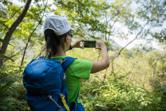 Backpacker taking picture with smartphone in sunny tropical rainforest