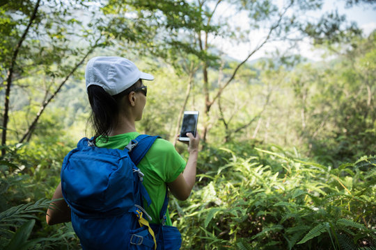 Backpacker taking picture with smartphone in sunny tropical rainforest