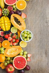 Top view of rainbow colored fruits, strawberries blueberries, mango orange, grapefruit, banana papaya apple, grapes, kiwis on the grey wood background, copy space for text, selective focus