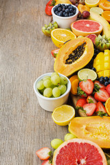 Variety of fruits, strawberries blueberries, mango orange, grapefruit, banana papaya apple, grapes, kiwis on the grey wood background, copy space for text, selective focus