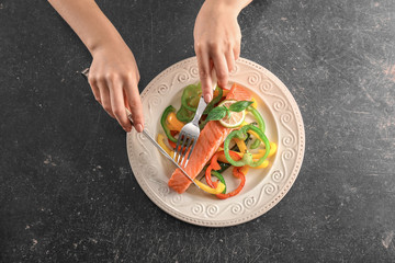Woman eating tasty salmon with fresh peppers on dark background