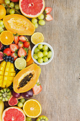 Above view of fruits, strawberries blueberries, mango orange, grapefruit, banana papaya apple, grapes, kiwis on the grey wood background, copy space for text, selective focus