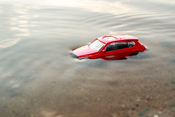 large view of a red toy car that drowned under water sticking one roof, green water and sand on the...