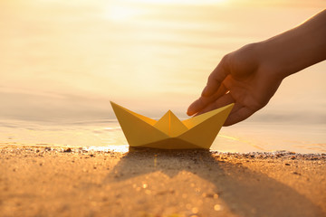 Woman putting origami boat on water surface near bank