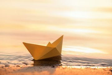 Origami boat on water surface near bank