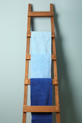 Clean towels hanging on ladder near grey wall