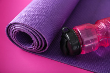 Yoga mat and bottle of water on color background