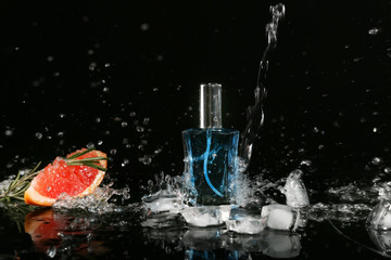 Fototapeta na wymiar Pouring of water on bottle with perfume, ice cubes and grapefruit against black background