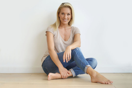 Beautiful blond woman sitting on floor against white wall