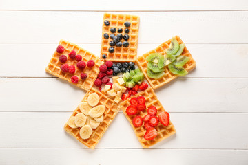 Delicious waffles with fruits and berries on white wooden background