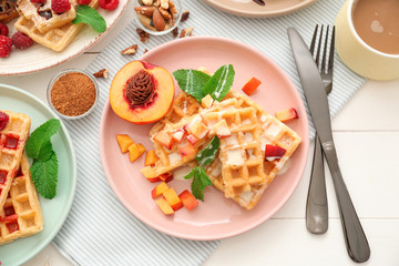 Plate with delicious waffles and peach slices on table