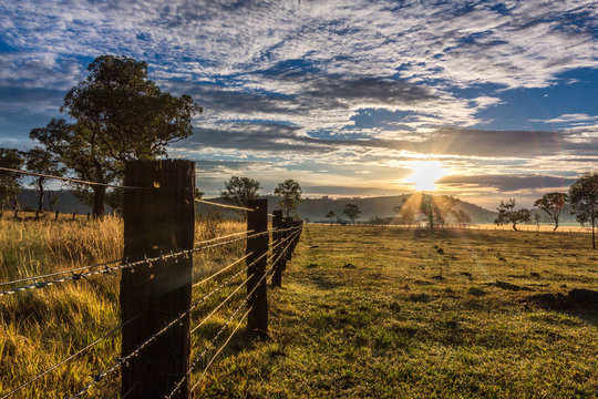 Country timber post fence line leading to sunrise and cloudy sky