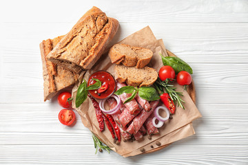 Board with slices of smoked sausages, sauce and bread on light wooden table