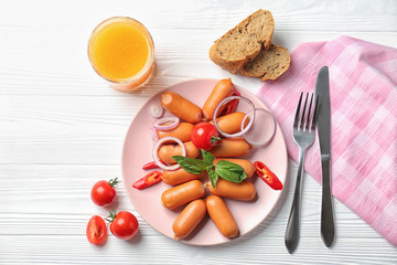 Plate with tasty sausages and glass of juice on light wooden table