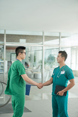 Young handsome doctor shaking hand of coworker who is replacing him