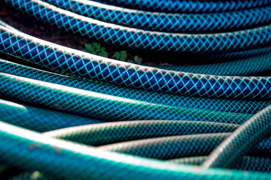 Green long hose pipe lying at the ground at natural background with bokeh